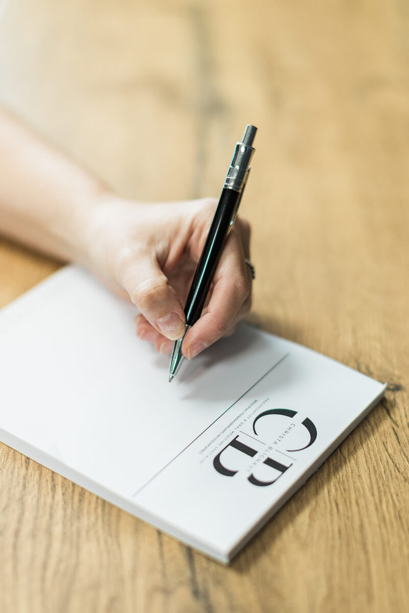 A hand writing on a notepad bearing the practice CB monogram.